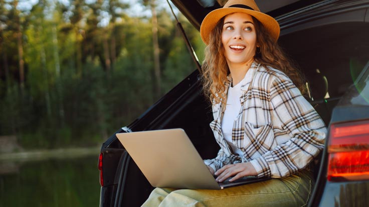 Woman sitting in the back of her SUV checks her laptop.